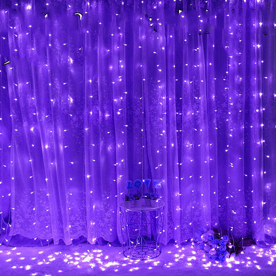 Purple LED string light curtain with a small round table and decorative items underneath.