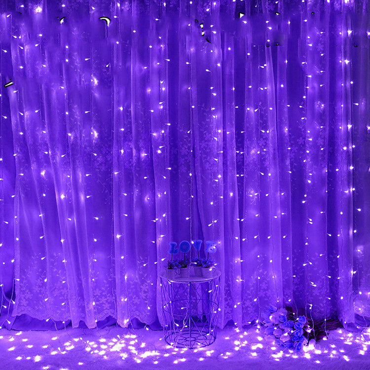 Purple LED string light curtain with a small round table and decorative items underneath.